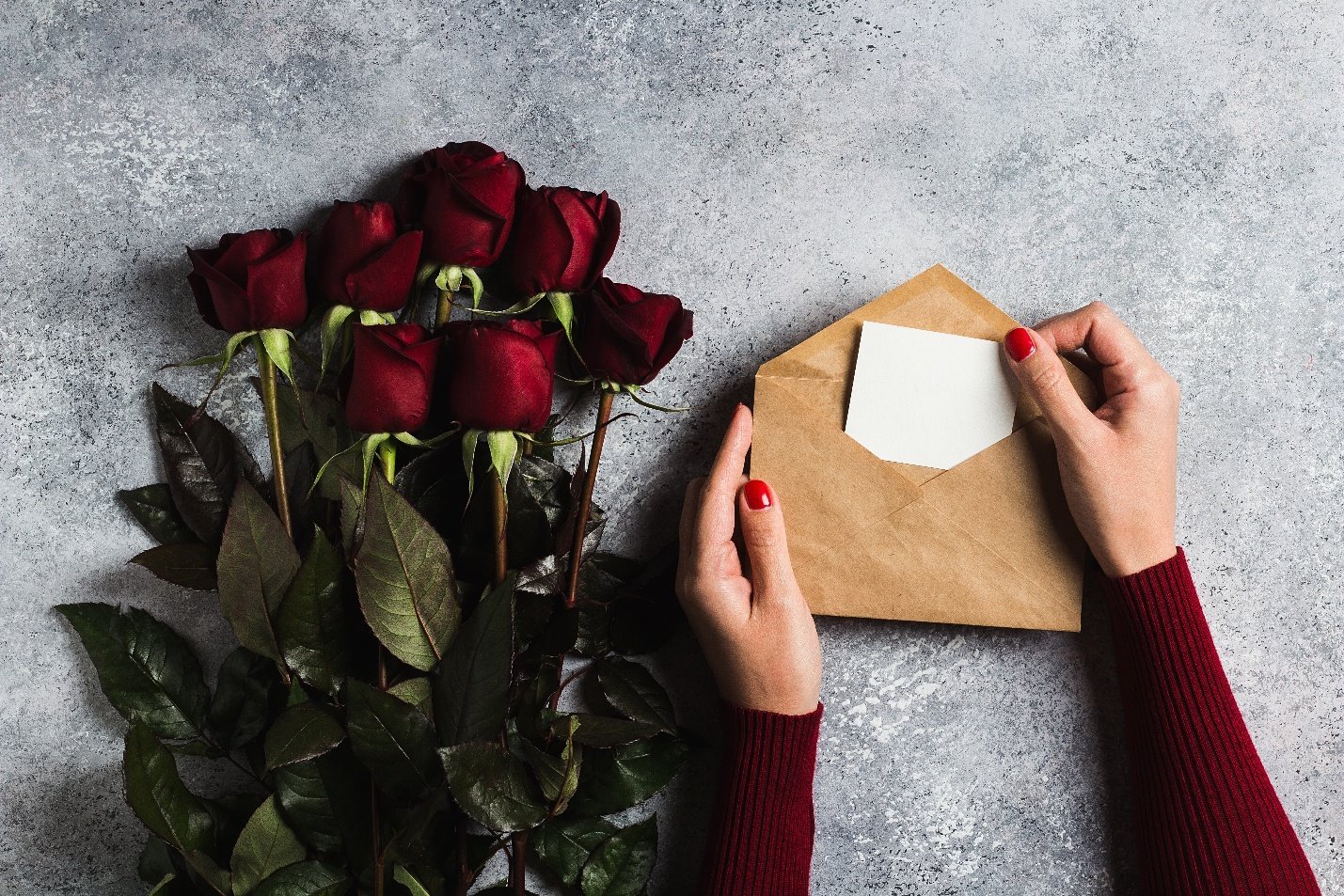 Hands holding an envelope beside a bouquet of red roses